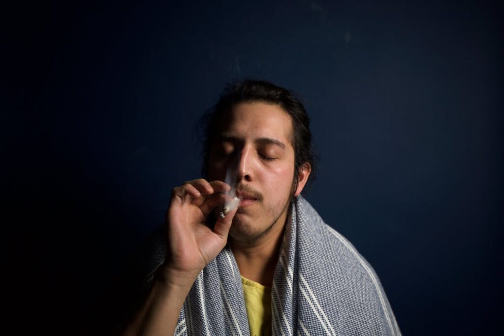 man-smoking-a-cigarette-395087 Close-up of a young man comfortably smoking in a dimly lit room, reflecting relaxation.